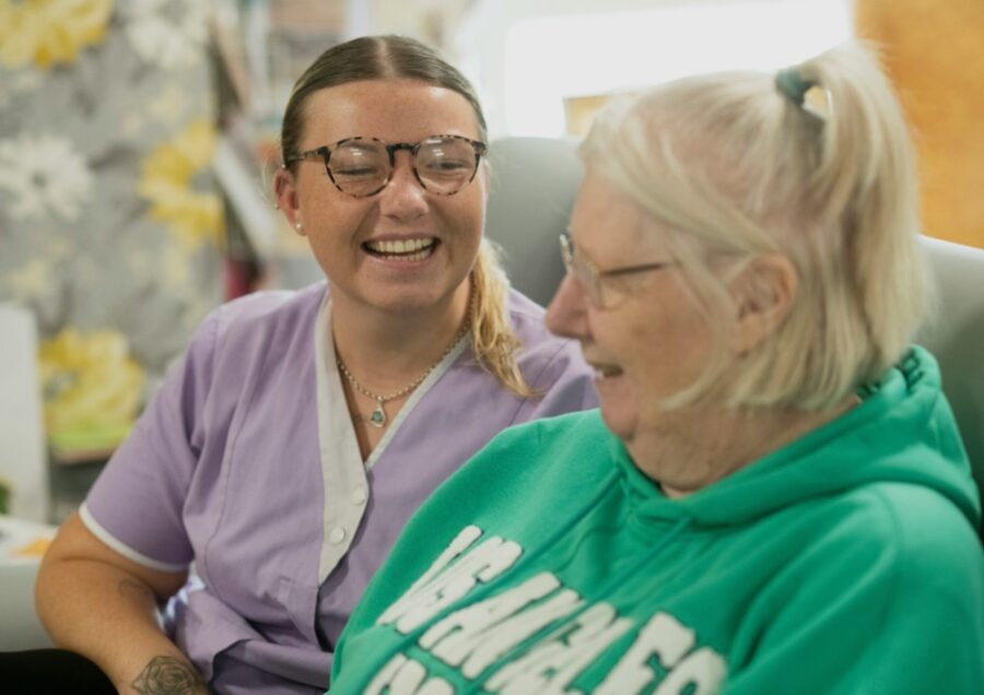 A smiling carer sitting and laughing with an older woman