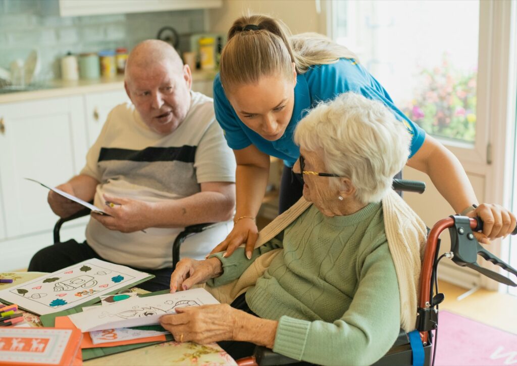 A carer leaning in to help two older residents with a puzzle